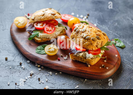 Zwei Brötchen mit Frischkäse, Cherry-Tomaten und Rucola auf ein Holzbrett. Gesunde Ernährung Stockfoto