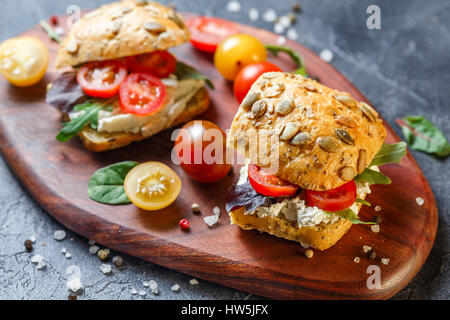 Zwei Brötchen mit Frischkäse, Cherry-Tomaten und Rucola auf ein Holzbrett. Gesunde Ernährung Stockfoto