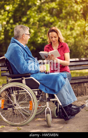 junge Frau Buch im Freien ihr behinderten Vater im Rollstuhl Stockfoto