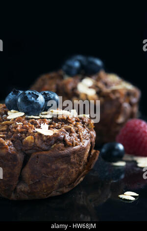 Schokoladen-Muffins mit Himbeeren, Bluesberries und Hafer auf dunklem Hintergrund. Stockfoto