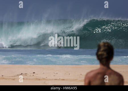 Ein junger Mann wacht eine Surfer fangen eine große Ozeanwelle Welt berühmten Banzai Pipeline auf der North Shore von Oahu Hawaii USA Stockfoto