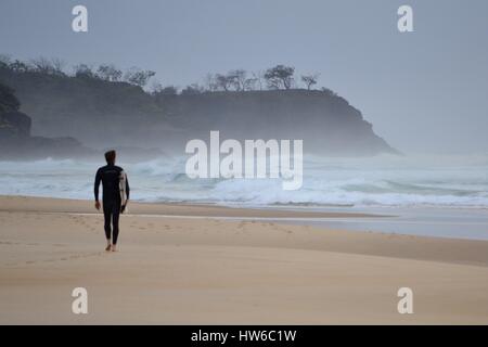 Einsamer Surfer am Strand in Australien an stürmischen Tag mit großer surfer Stockfoto