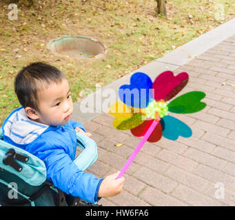 Kleinkind Jungen spielt Windrad während der Fahrt in Kinderwagen Stockfoto