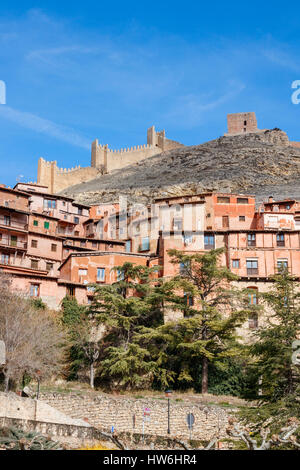 Häuser und Straßen von Albarracin gegen den Hang des Hügels mit der Stadtmauer auf der Oberseite an einem sonnigen Tag unter einem blauen Himmel. Albarracin, Teruel, Spanien. Stockfoto
