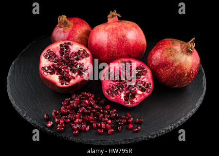 Drei Granatäpfel und Samen auf schwarze Platte mit schwarzem Hintergrund Stockfoto