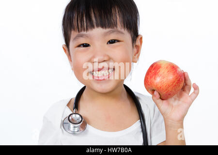 Asiatische kleine chinesische Mädchen verkleidete sich als Arzt mit einem Stethoskop hält einen Apfel isoliert auf weißem Hintergrund Stockfoto