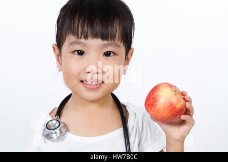 Asiatische kleine chinesische Mädchen verkleidete sich als Arzt mit einem Stethoskop hält einen Apfel isoliert auf weißem Hintergrund Stockfoto