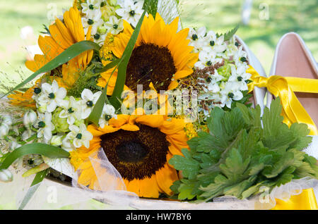 Brautstrauß von Wildpflanzen, Geranien, Sonnenblumen und Brautschuhe. Stockfoto