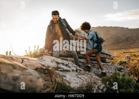 Junger Mann hilft Freund zu dem Felsen erklimmen. Junges Paar Wanderungen in der Natur. Stockfoto