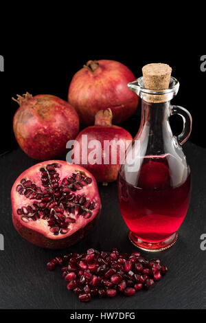 Drei Granatäpfel, Samen und Flasche Saft auf schwarze Platte mit schwarzem Hintergrund Stockfoto