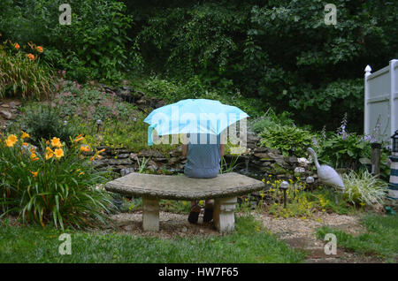 Ein junges Mädchen sitzt auf einer Bank unter einem Regenschirm, Fische im Teich beobachten. Stockfoto