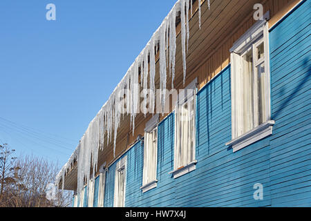 Gefährliche Eiszapfen hängen vom Dach eines Holzhauses Stockfoto