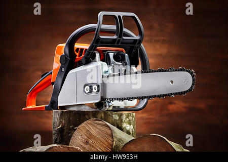 Schneiden Sie Protokolle Feuerholz und Kettensäge auf braunem Hintergrund aus Holz. Erneuerbare Ressource Energie. Holzbearbeitung. Leistung und kraftvoll. Detail der orange Chai Stockfoto