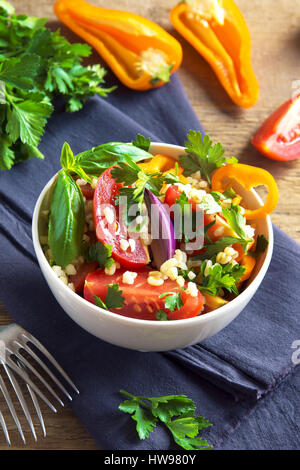Frische Bio-Tomaten und Bulgur Couscoussalat Taboulé mit Gemüse und grünen - gesunde vegetarische vegane Ernährung traditionellen Salat auf rustikal aus Holz Stockfoto