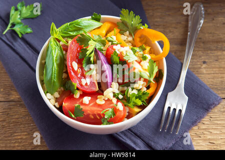 Frische Bio-Tomaten und Bulgur Couscoussalat Taboulé mit Gemüse und grünen - gesunde vegetarische vegane Ernährung traditionellen Salat auf rustikal aus Holz Stockfoto