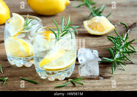 Alkoholische Getränke (Gin Tonic Cocktail) mit Zitrone, Rosmarin und Eis am rustikalen Holztisch, Textfreiraum Stockfoto