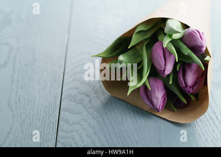 violette Tulpen in Kraftpapier auf blauem Hintergrund Holz Stockfoto