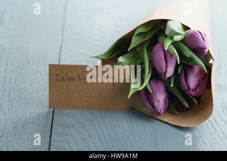 violette Tulpen in Kraftpapier auf blauem Hintergrund Holz Stockfoto