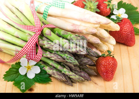 Spargel-Nahaufnahme. Frischer grüner und weißer Spargel mit Erdbeeren auf Holz Stockfoto