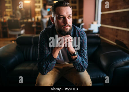 Bärtiger Mann sitzen auf einer Couch in der Barbershop. Friseur Salon Interieur auf Hintergrund Stockfoto