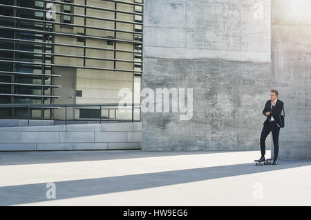 Voller Länge Schuss eines Geschäftsmannes steht auf einem Skateboard, denken Stockfoto