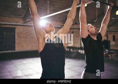 Sportlicher Mann und Frau Klimmzüge in moderne geräumige Turnhalle zu tun. Stockfoto
