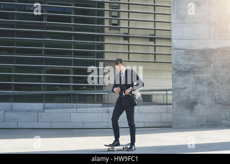 Vorderansicht eines Geschäftsmannes Anpassung seine Tasche auf Skateboard stehend Stockfoto