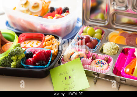 Mama packt eine glückliche Anmerkung der Ermutigung mit einer bunten Bento Lunch Box verpackt mit gesunden Früchten, Gemüse und snacks Stockfoto