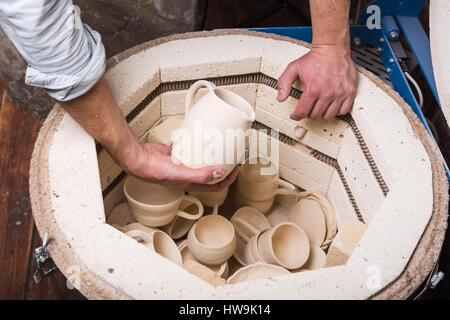 Geröstete keramische Produkte ohne Glasur in des Töpfers Hand hautnah. Ansicht von oben. Kunst und Geschäft, Hobby und freiberufliche Arbeitskonzept. Keramik Brennofen für den Brennvorgang bereit machen. Stockfoto