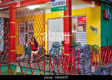 Amerika, Karibik, Kuba, Pinar del Rio, Vinales, Weltkulturerbe von UNESCO, Vinales, Frau sitzt vor seiner sehr bunten Haus Stockfoto