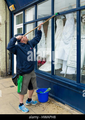 Mann, die Reinigung ein Fenster auf einen kleinen Kleid Shop Geschäft in North Yorkshire Stockfoto