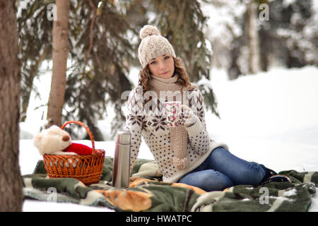 Schöne Mädchen sitzt auf einer Decke im Winter im Wald, Fosest und Tee trinken, ist gut, Spaß, lustig, glückliche Zeit, Datum, Picknick. Stockfoto