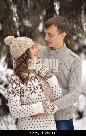 Gut aussehender Mann Kuss auf die Stirn ihres Geliebten, schön, hübsch, fröhlich, glücklich, verliebt, lächelnde Mädchen mit Pullover, Handschuhe und Hut, Winter, Schnee, Kälte Stockfoto