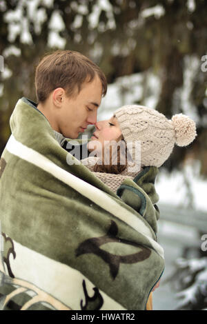 Gut aussehender Mann Kuss auf die Stirn, ihre Geliebte, schöne, hübsche, attraktive Mädchen mit Pullover, Handschuhe, Winter, Kälte, Schneewald, Hütte, Liebe, glücklich, Stockfoto