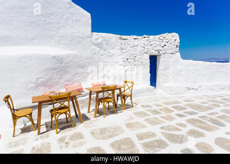 Stühle, Schreibtisch und eine blaue Tür auf eine weiß getünchte Mykonos Altstadt Straße, Griechenland Stockfoto