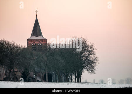 Turm der Kirche erhebt sich über eine Reihe von Bäumen in einem typischen kleinen niederländischen Dorf hinter dem Deich in der Wintersaison Stockfoto