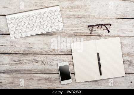 Arbeiten statt Blick von oben: Tastatur, Buch, Handy, Brille auf hölzernen Hintergrund Stockfoto