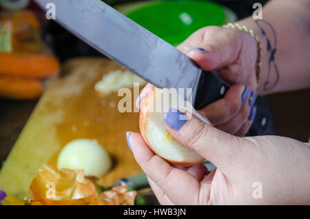 Ein Blick auf eine Frau mit einem großen Messer zu schälen und Zwiebel im Rahmen der Vorbereitung einer Mahlzeit die Hände. Stockfoto