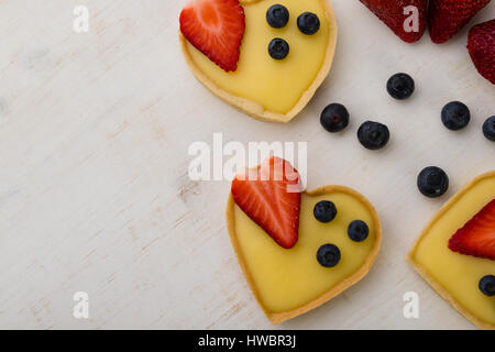 Herz Form Vanille Torte mit Erdbeeren und Heidelbeeren auf weißen Tisch Stockfoto