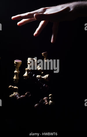 Eine Hand, die Schachfiguren auf dem Boden, vor schwarzem Hintergrund isoliert fallen zu lassen Stockfoto