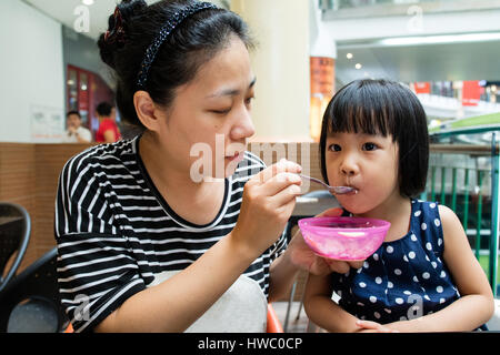 Asiatische Mutter füttert ihre Tochter im Café im freien Stockfoto