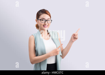 junge attraktive asiatische Geschäftsfrau verweist auf den Finger auf grauem Hintergrund Stockfoto