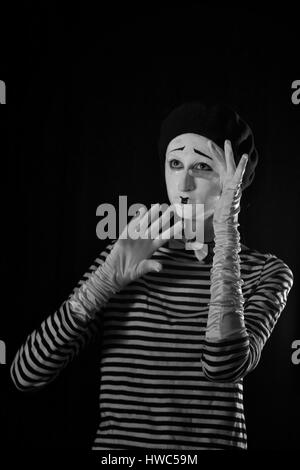 Emotionale professionelle Mime in abgespeckte Blacn und weißen Hemd mit schwarze Kappe und weiße Fliege stehen vor schwarzem Hintergrund im Zirkus Stockfoto