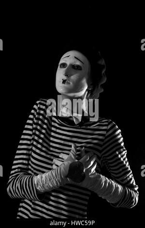 Emotionale professionelle Mime in abgespeckte Blacn und weißen Hemd mit schwarze Kappe und weiße Fliege stehen vor schwarzem Hintergrund im Zirkus Stockfoto