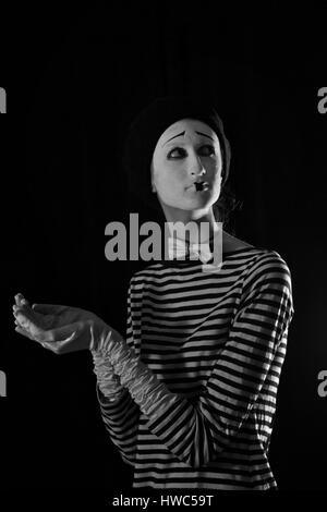 Emotionale professionelle Mime in abgespeckte Blacn und weißen Hemd mit schwarze Kappe und weiße Fliege stehen vor schwarzem Hintergrund im Zirkus Stockfoto