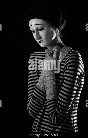 Emotionale professionelle Mime in abgespeckte Blacn und weißen Hemd mit schwarze Kappe und weiße Fliege stehen vor schwarzem Hintergrund im Zirkus Stockfoto