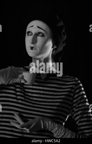 Emotionale professionelle Mime in abgespeckte Blacn und weißen Hemd mit schwarze Kappe und weiße Fliege stehen vor schwarzem Hintergrund im Zirkus Stockfoto