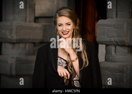 Erstaunlich, hübsches weißes Lächeln. Schöne Mädchen gegen Steinmauer mit schwarzen Jacke steht lächelnd Stockfoto