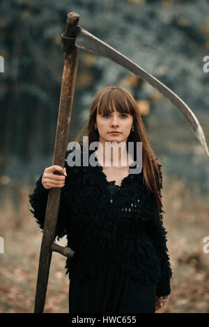 Nahaufnahme Bild ziemlich ernst schönes Mädchen mit langen Haaren in schwarzer Kleidung mit Zopf auf dunklen Wald Hintergrund. Ernsthafte mystische Mädchen mit seri Stockfoto