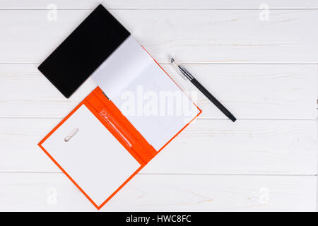 Offene leere Seite ein orange Tagebuch mit einem Stift für die Terminvereinbarung, organisieren einen Zeitplan und Handy auf weißer Holztisch Stockfoto